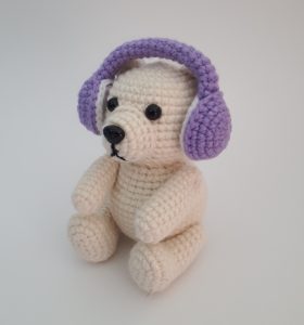 Crocheted polar bear wear a set of purple crocheted earmuffs.